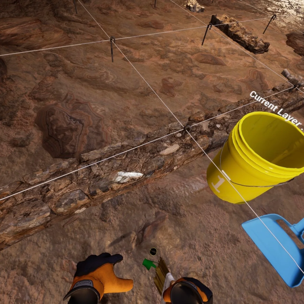 First-person view of gloved hands holding a brush beside a string excavation grid, a yellow bucket, and a blue dustpan.